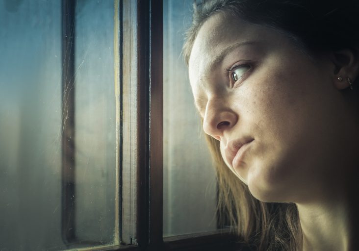 A teenager girl looking away through a window at home, thinking, sad.